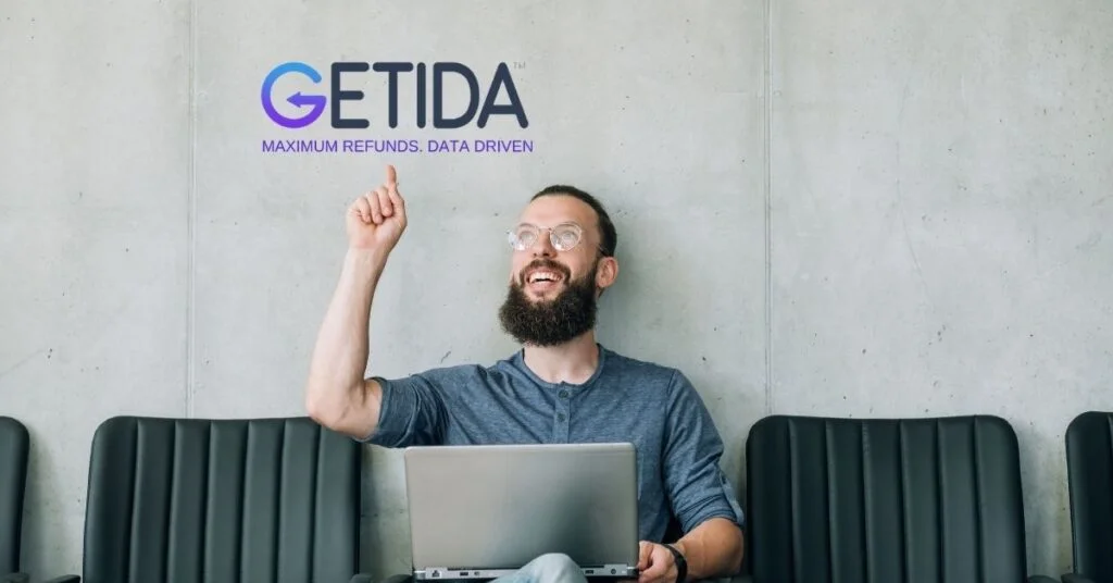 Person in grey t-shirt sitting with laptop near GETIDA logo.