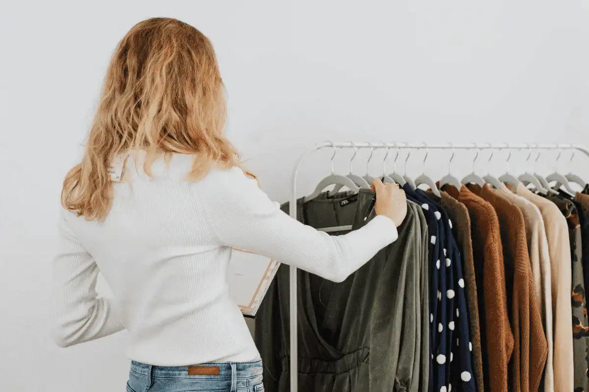 Woman browsing through a selection of clothes on a rack in a bright room.